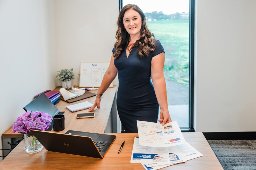 SEO strategist standing in a modern office with campaign planning documents and a laptop, representing Inner Loop Media's SEO services